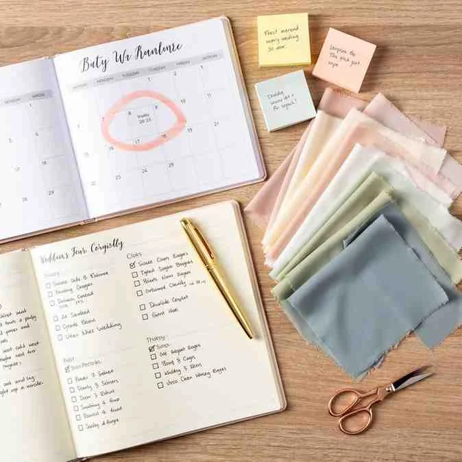 A wedding planning notebook, calendar, and swatches laid out on a table